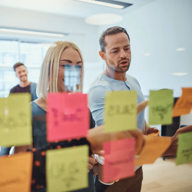 Team in modernem Büro mit Glaswand, Frau und Mann mit farbigen Haftnotizen, Brainstorming-Szenario