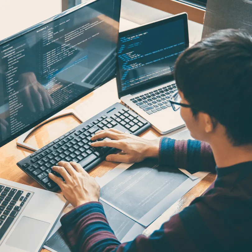 Programmierer sitzt vor mehreren Bildschirmen mit Code, arbeitet an Tastatur