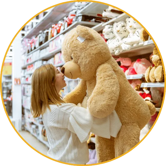 Mädchen mit Teddybär im Spielwarengeschäft vor Regalen mit gelbem Rahmen