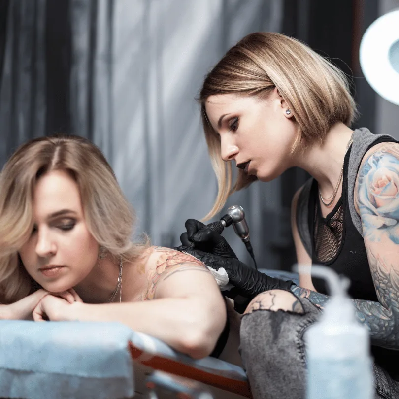 Tätowiererin tätowiert weibliche Kundin an der Schulter in Tattoostudio-Setting