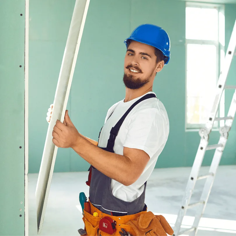 Junger Handwerker mit blauem Helm hält PVC-Profil auf Trockenbau-Baustelle