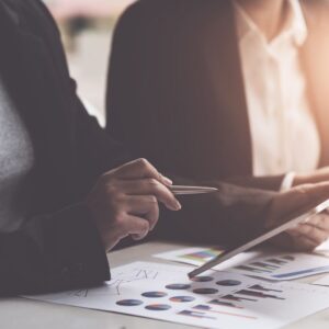 Nahaufnahme von Händen mit Stift über Business-Diagrammen und Analysen auf Schreibtisch