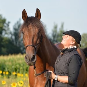 Nicole Weinauge neben braunem Pferd in Feld mit Blüten, Porträt