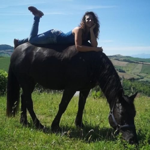 Julia Reyam liegt auf schwarzem Pferd auf Wiese, Landschaftshintergrund