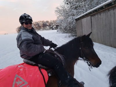 Frau im schwarzen Helm sitzt auf schwarzem Pferd im Schnee