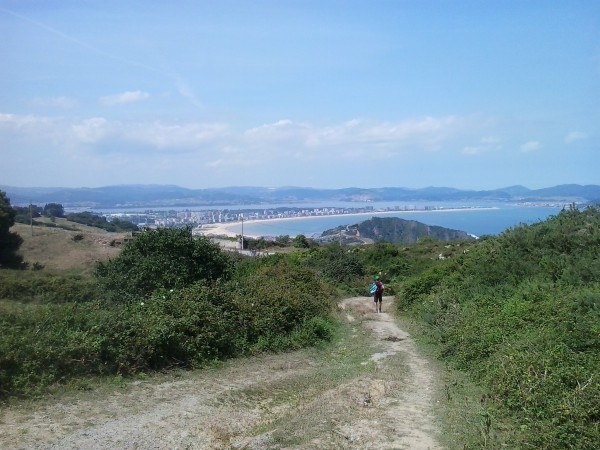 Wanderer auf Pfad mit Ausblick auf Küste und Bucht mit Stadt