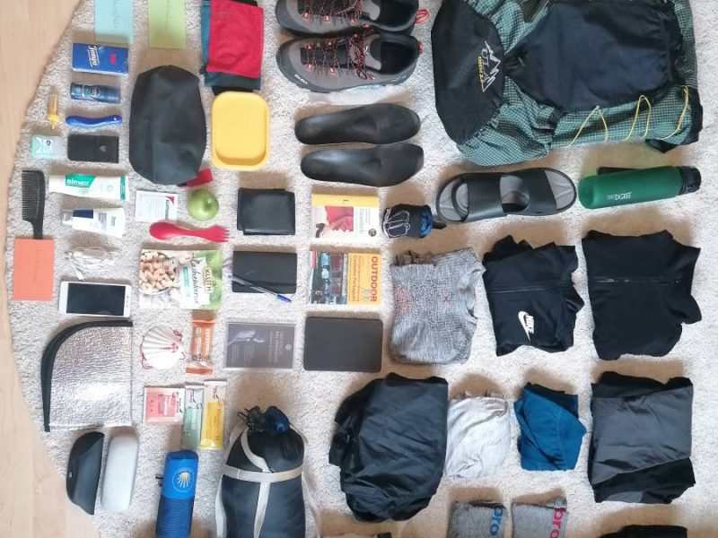 Jakobsweg Packliste mit ausgebreiteten Wanderausrüstungen und Gepäck