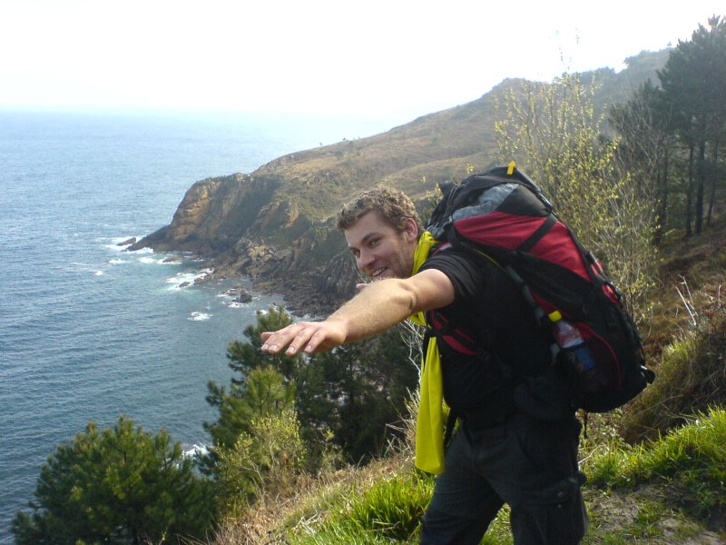 Christoph mit ausgebreiteten Armen und Rucksack glücklich auf Küstenweg