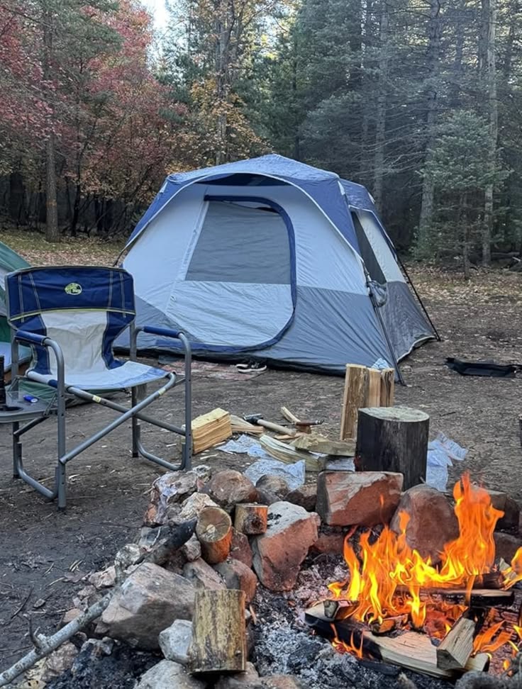 Campingszene mit blauem Zelt, Lagerfeuer und Campingstuhl im Wald