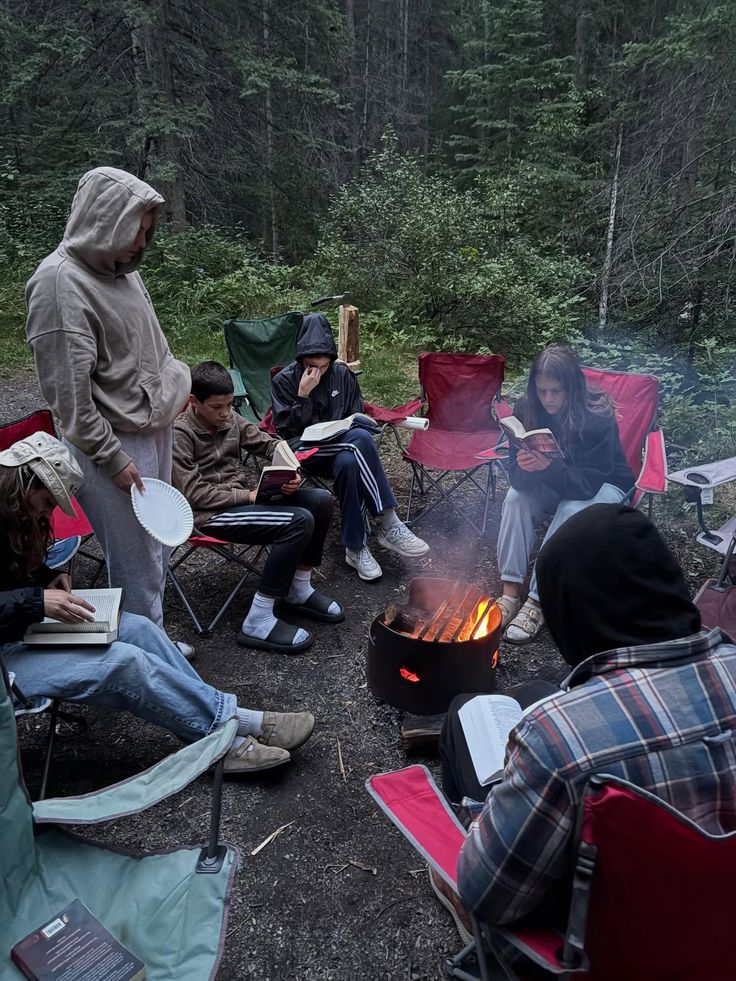Gruppe Menschen am Lagerfeuer im Wald beim Camping und Lesen