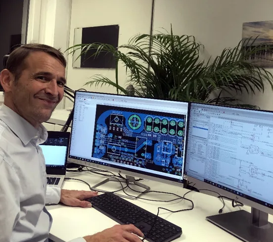 Mann am Schreibtisch mit Dual-Monitor-Setup zeigt technische Steuerungszeichnung auf großem Monitor
