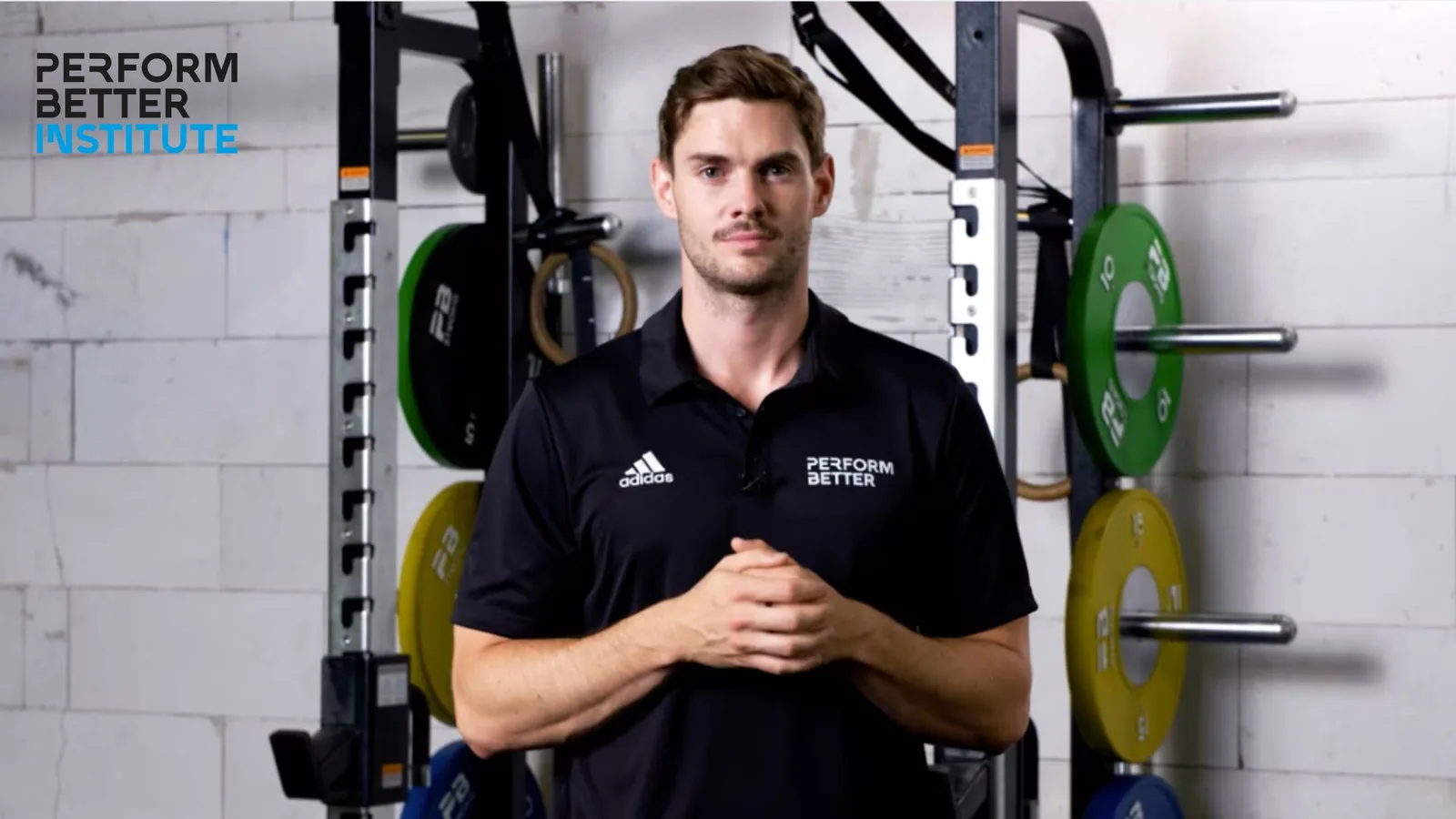 CFT – Functional-Training-Kurs 6 Trainer in schwarzem Adidas PerformBetter Polo-Shirt vor Trainingsgeräten mit Gewichtsplatten im Gym
