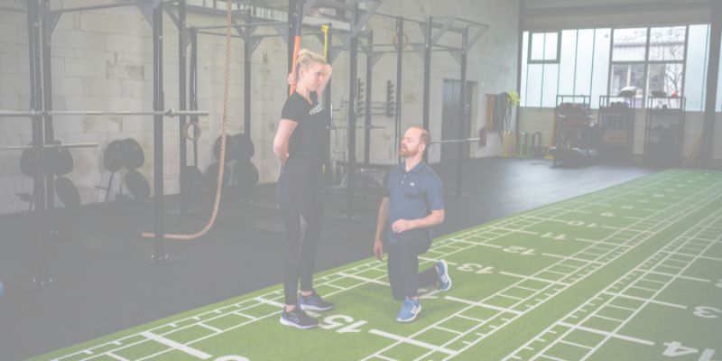 CFT – Functional-Training-Kurs 3 Trainer demonstriert Seilübung mit Klient im modernen Gym auf grünem Trainingsboden
