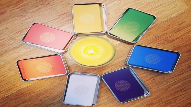 Acht farbige Chakra-Scheiben in Metallrahmen auf Holzoberfläche angeordnet, zentral gelbe runde Scheibe, identisch mit Bild 1