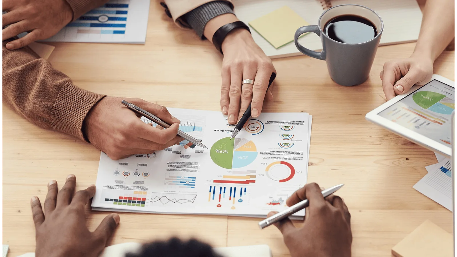 Mehrere Personen am Holztisch analysieren Geschäftsdiagramme und Statistiken auf Papier, Tablet und Tasse Kaffee
