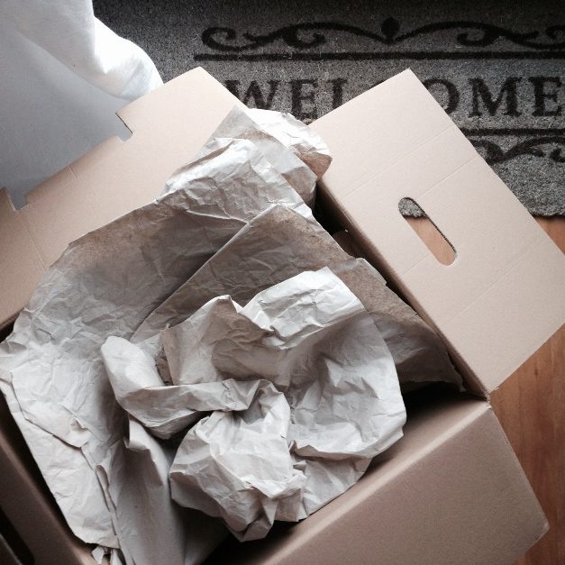 Offener Umzugskarton mit Packpapier und weißen Griffen auf Fußmatte
