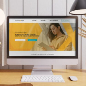 Monitor zeigt Website mit gelb-orangem Hero-Bereich und Frau mit Tablet