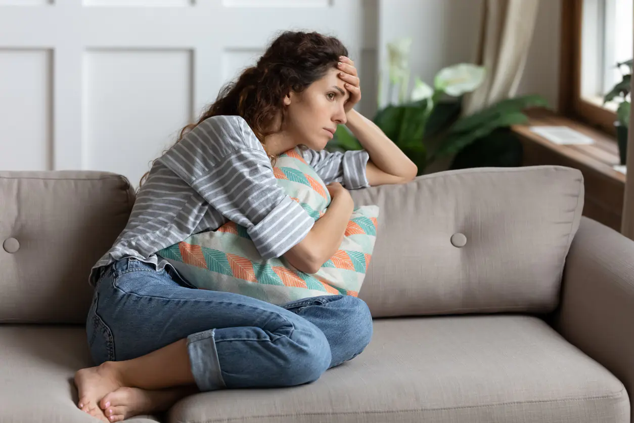 Chronisch gesund mit Vitalstoffpower – Videokurs über Vitalstoffe 4 Frau sitzt erschöpft auf Sofa, hält sich die Stirn, wirkt müde und gestresst
