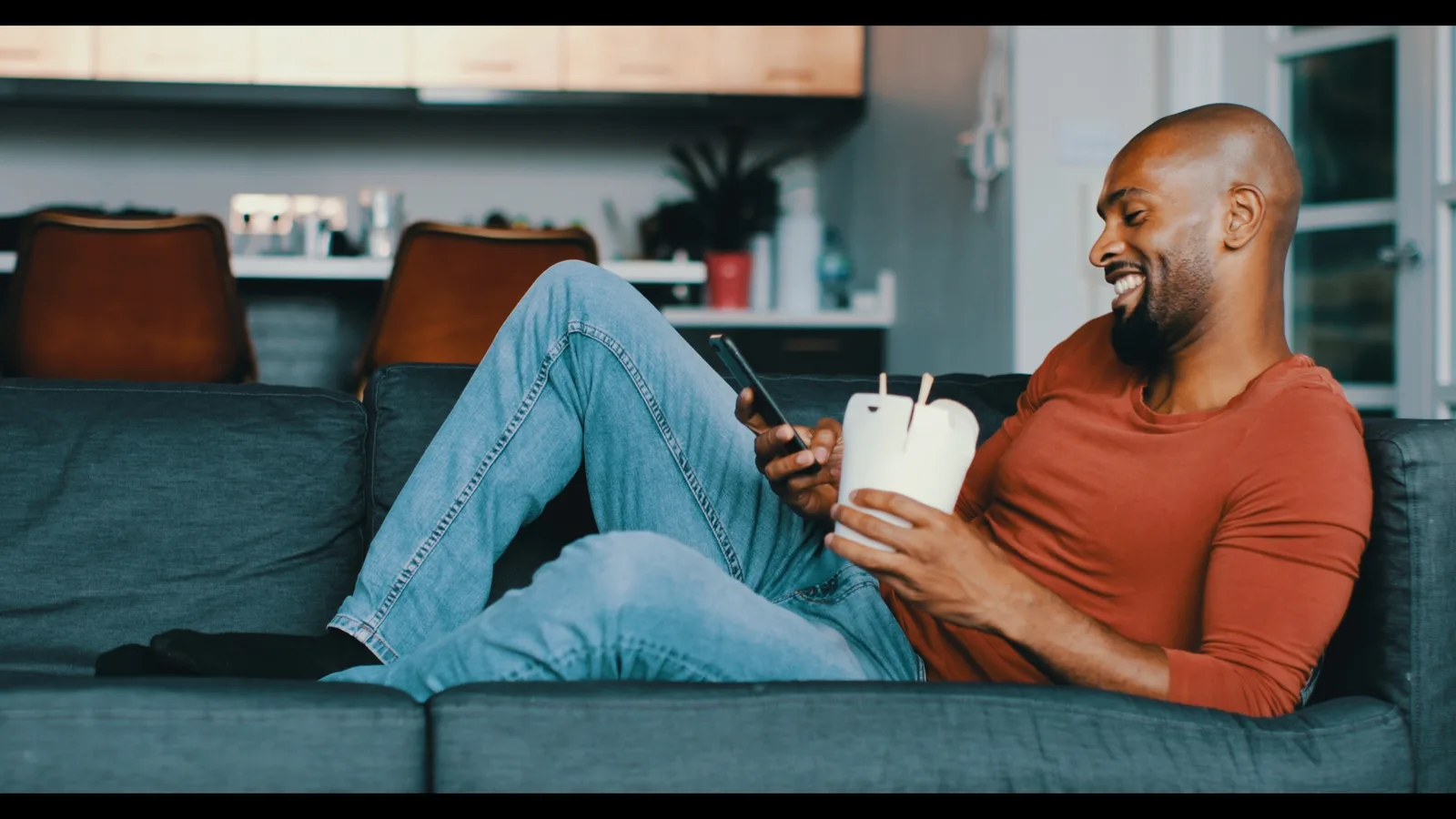 Mann auf Sofa mit Smartphone und Kaffeebecher, Teal & Orange Color-Grading Look