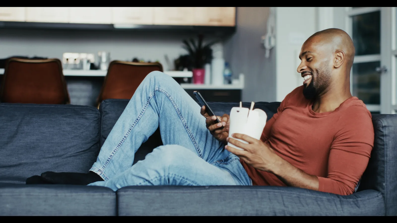 Mann auf Sofa mit Smartphone und Kaffeebecher, Fuji-Film Look Color-Grading