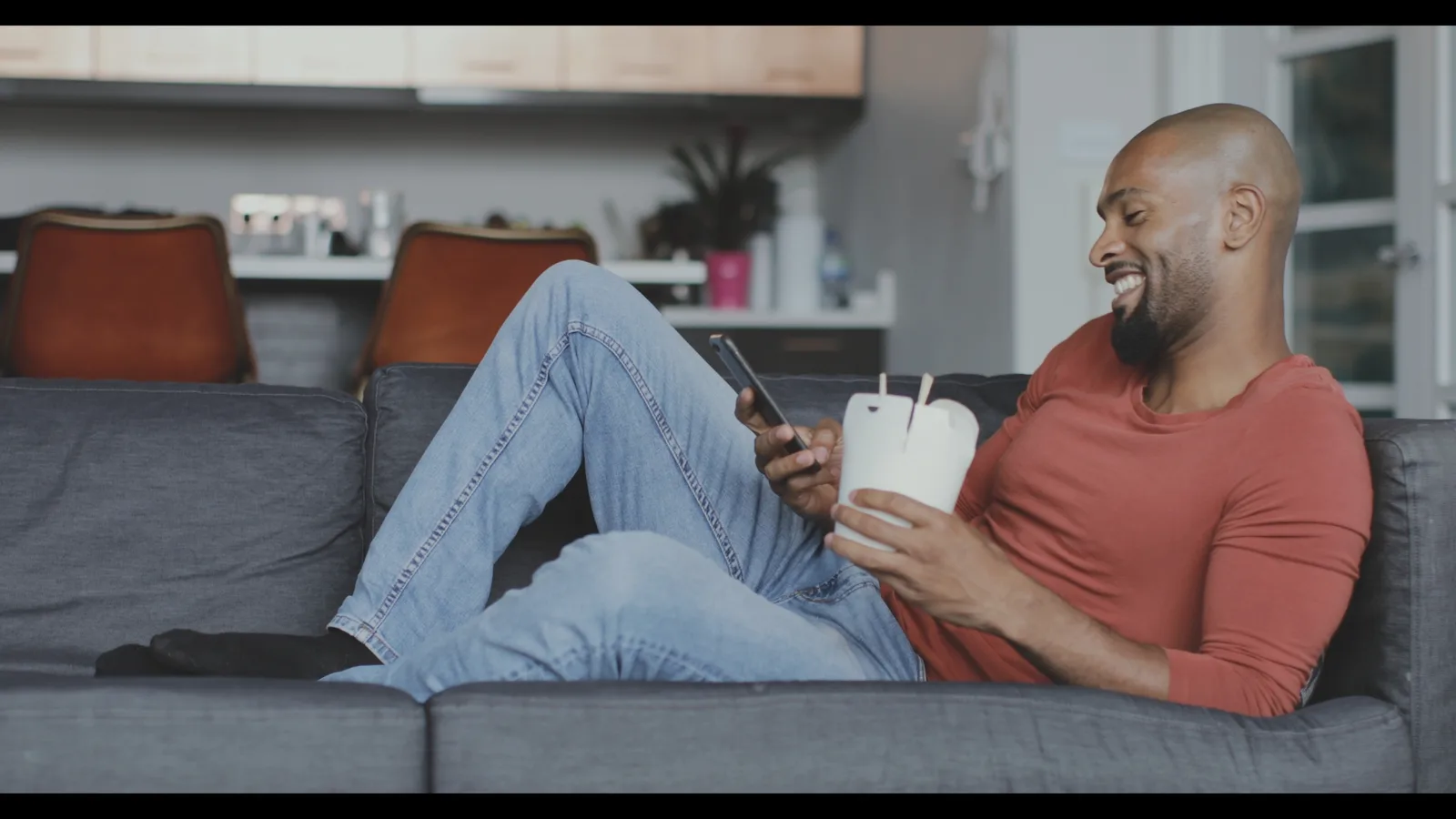 Mann auf Sofa mit Smartphone und Kaffeebecher, Original-Grading ohne Farbbearbeitung