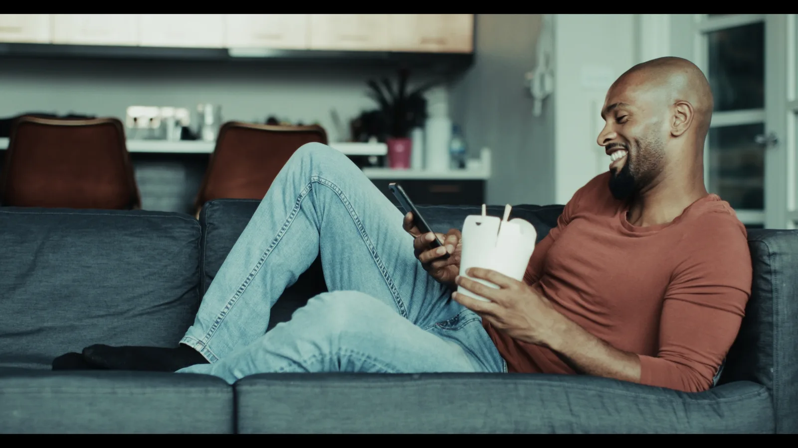 Mann auf Sofa mit Smartphone und Kaffeebecher, Bleach Bypass Color-Grading Look