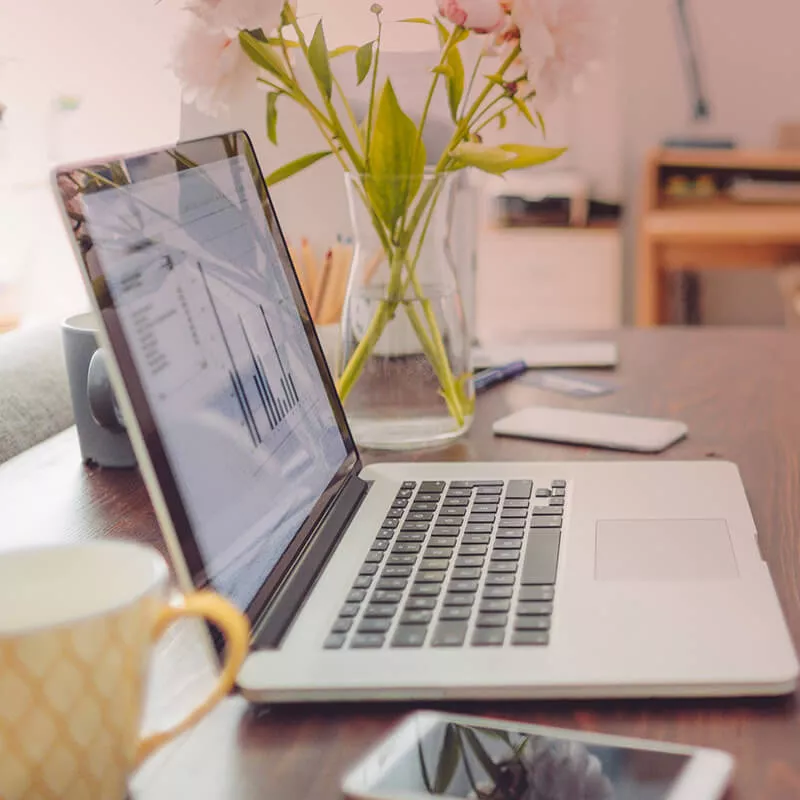 Laptop mit Tablet und Blumenstrauß auf Schreibtisch, Tasse und Notizen