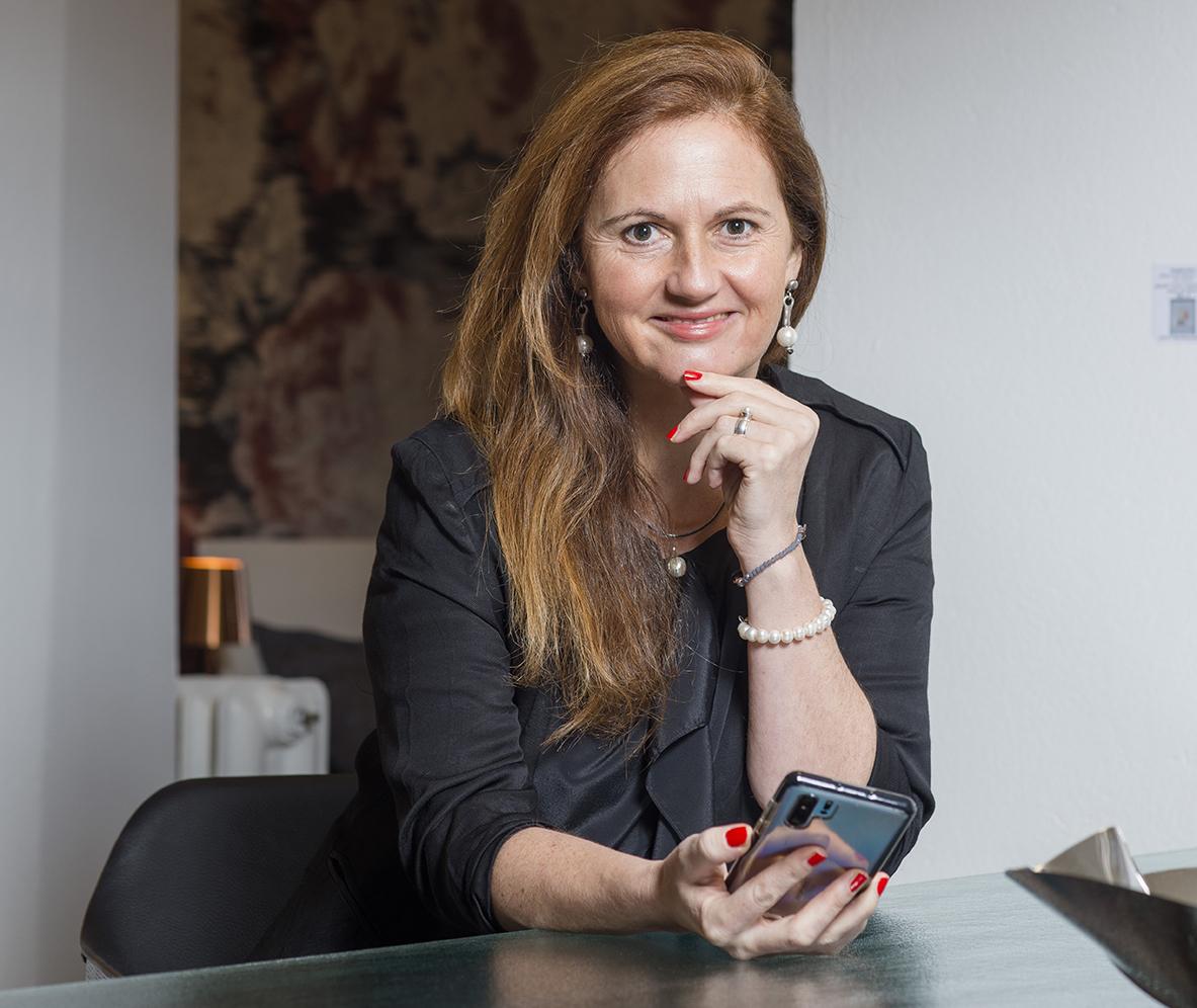 Porträt Natascha Heistrüvers mit Smartphone am Schreibtisch in heller Büroumgebung