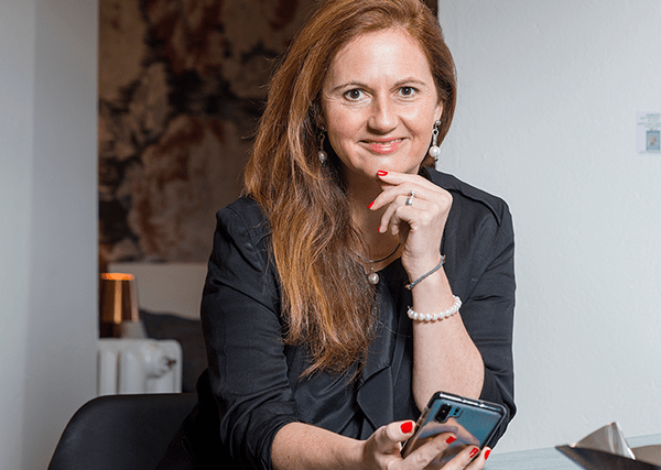 Porträt Natascha Heistrüvers mit Smartphone in Business-Kleidung am Schreibtisch