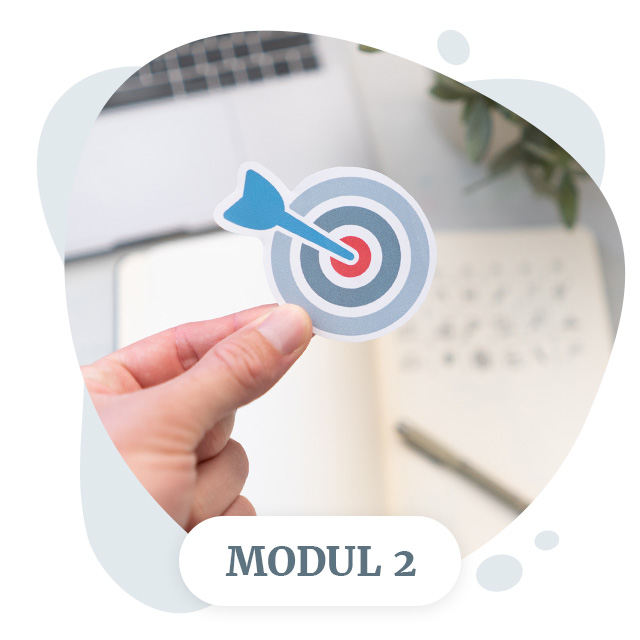 Hand hält Zielscheiben-Illustration mit Pfeil vor verschwommenem Hintergrund, Modul-2-Label