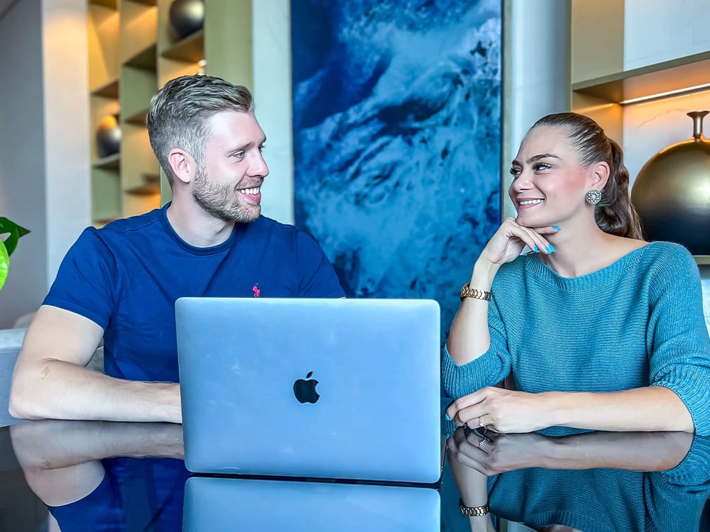 Mann und Frau lächeln sich an, arbeiten gemeinsam an silbernem Laptop
