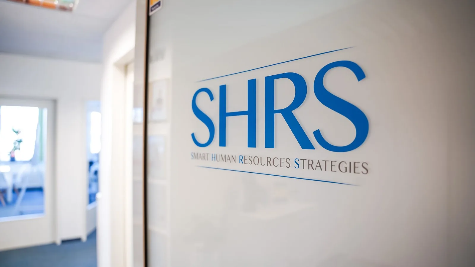 SHRS Logo an Bürowand: Smart Human Resources Strategies in blauer Schrift