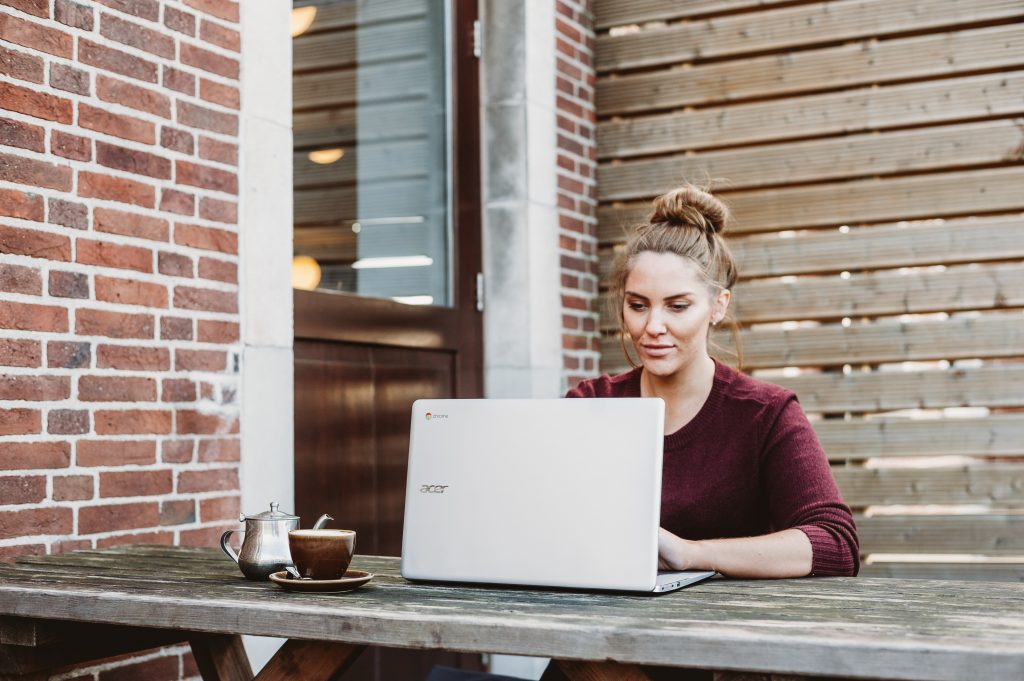 Das bewährte 7 Konten-Modell für Unternehmerinnen – Finanz-E-Book 5 Frau mit Laptop auf Holztisch vor Ziegelmauer, Kaffee, konzentriert arbeitend