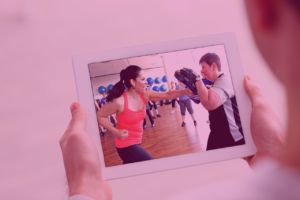 Hands halten Tablet mit Videostandbild von Personen beim Gruppentraining auf rosa Hintergrund
