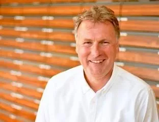 Portrait eines Mannes mit grauem Haar in weißem Hemd vor orangenem Hintergrund