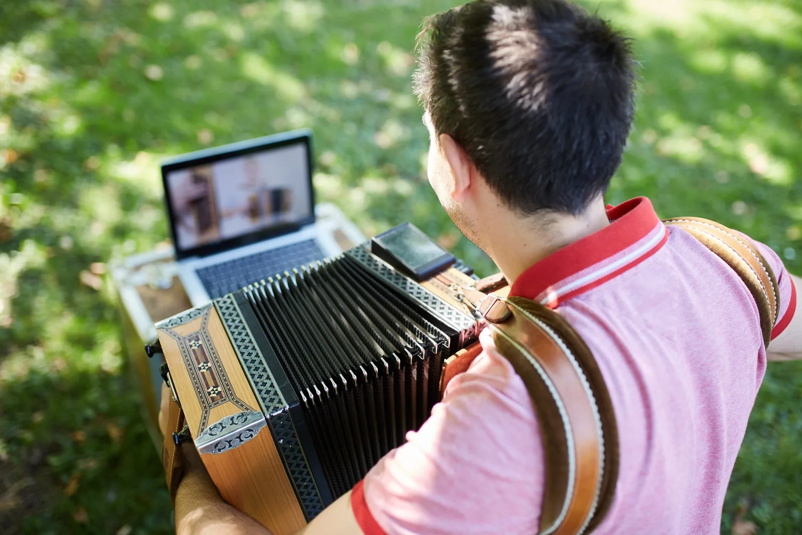 Thomas von hinten spielend an einer Harmonika, dabei Laptop mit Lernvideos im Hintergrund