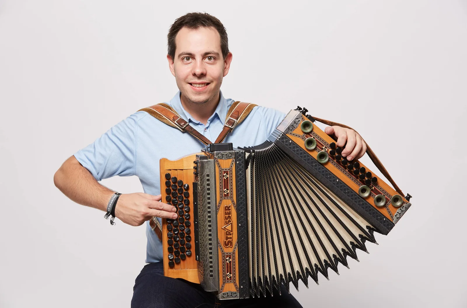Thomas Strasser mit orange-schwarzer Steirischer Harmonika im Porträt vor hellem Hintergrund