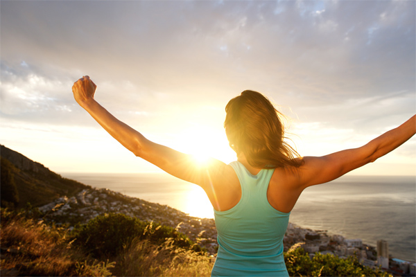 Low Carb – Abnehmkurs mit Ernährungsplan von OnVersum GmbH 15 Frau in Sportkleidung mit erhobenen Armen bei Sonnenaufgang am Meer mit Blick auf Landschaft