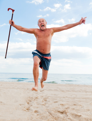 Älterer Mann joggt mit Laufstock am Strand mit ausgestreckten Armen