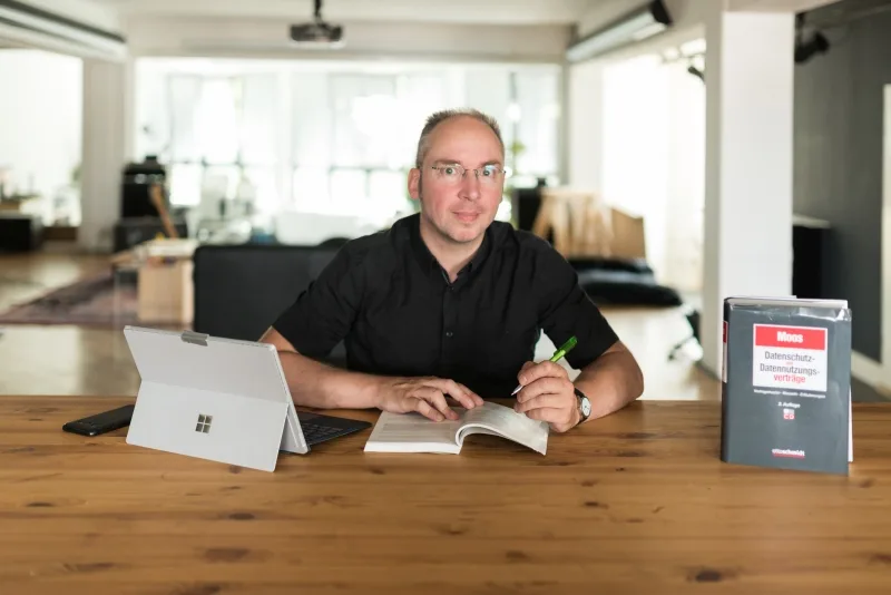 Lorenz Macke, Datenschutzbeauftragter, sitzt am Schreibtisch mit Laptop und Datenschutzbuch