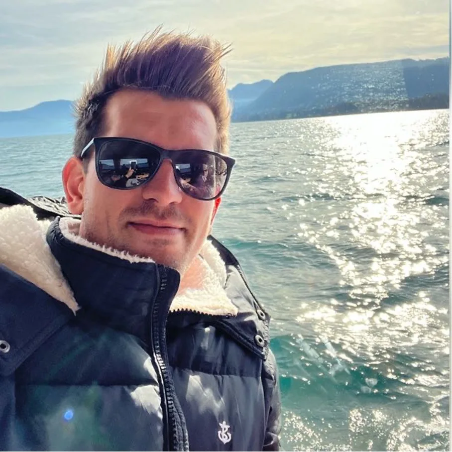 Kundenstimme: Mann mit Sonnenbrille am Wasser, Berglandschaft im Hintergrund