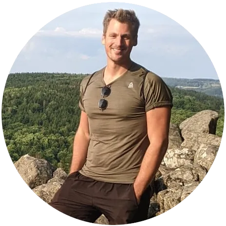 Junger Mann in olivgrünem T-Shirt auf Berg mit Wald im Hintergrund, kreisförmiges Porträtfoto