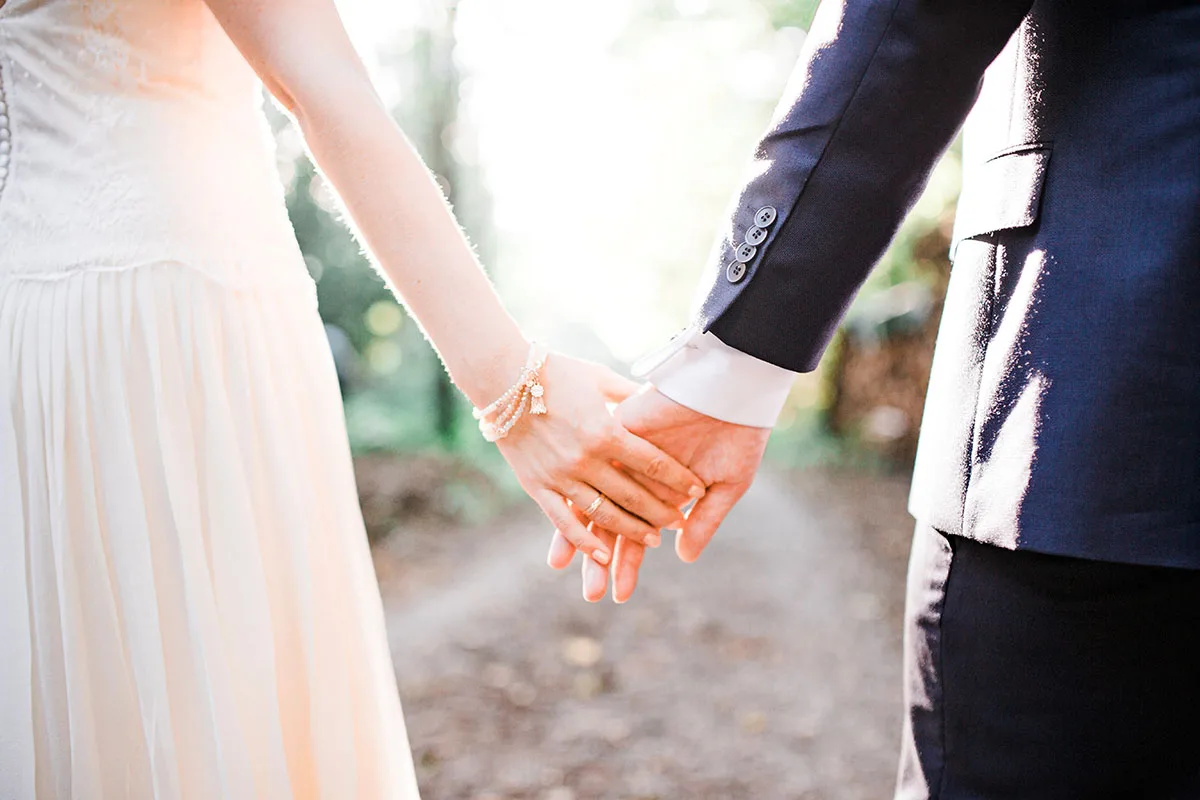 Hochzeitspaar hält sich an den Händen, Nahaufnahme mit Ringen und Hochzeitskleidung