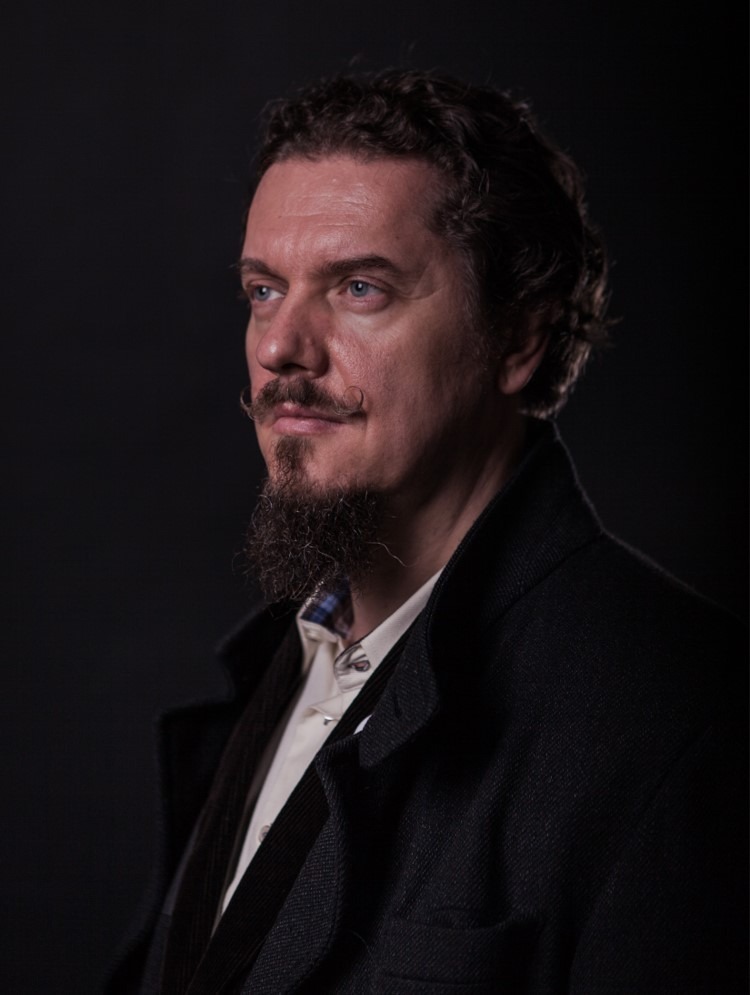 Porträt von Bernhard Reicher, Autor und Magier, mit dunklem Anzug vor schwarzem Hintergrund