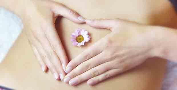 Frauenhände formen Herz über Bauch mit Gänseblümchen, Wunschgewicht Kurs