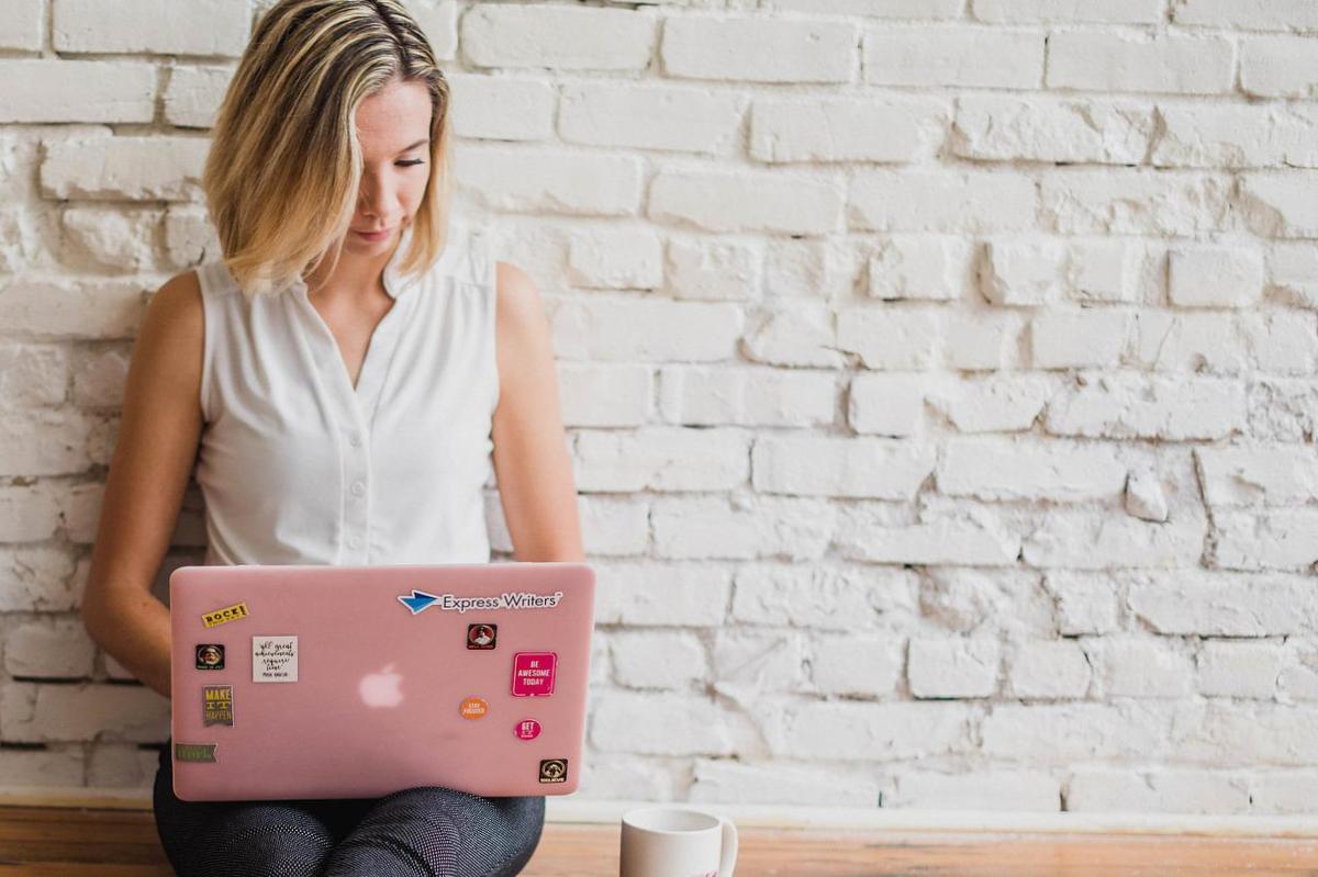 Frau mit rosa Laptop vor weißer Backsteinwand – Online-Arbeit und Influencer