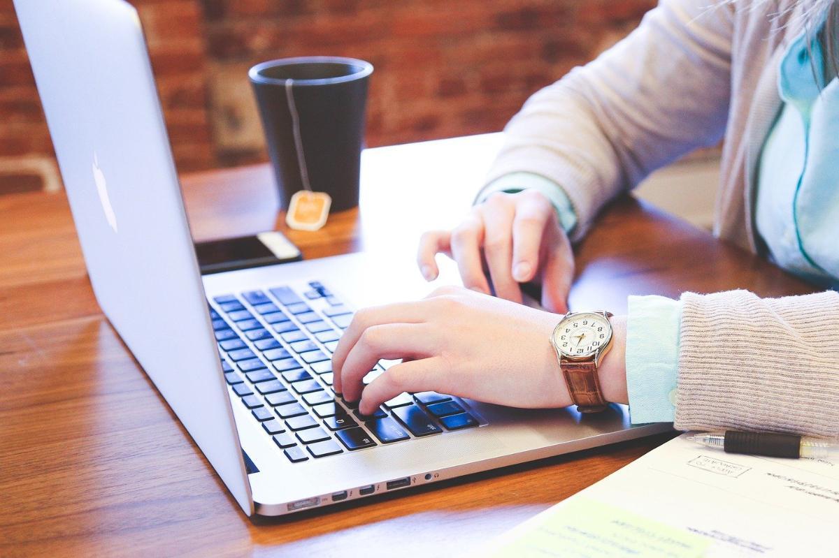 Hände tippen auf Laptop-Tastatur mit Kaffee und Notizbuch – Online-Lernen