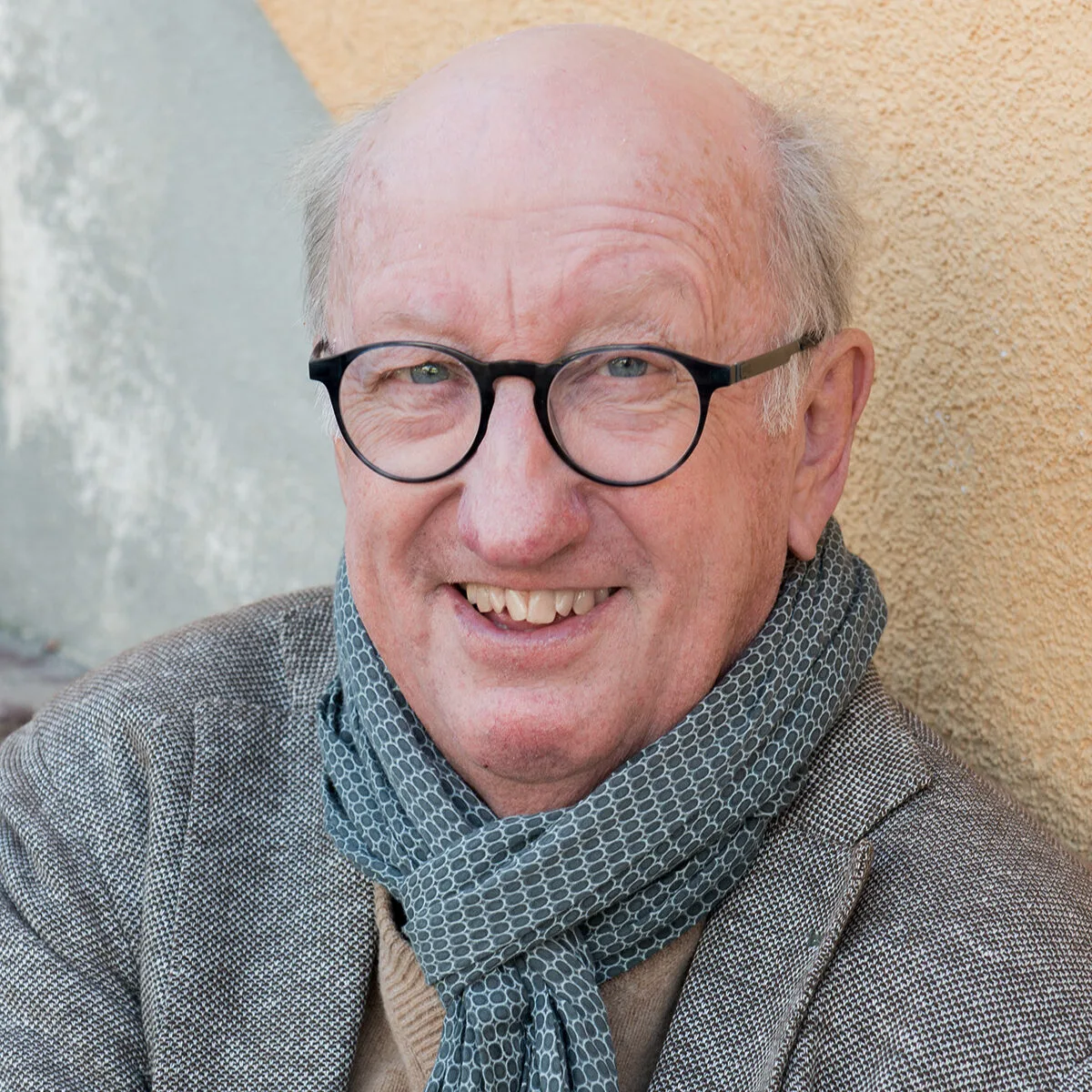 Älterer Herr mit Brille und grauem Haar, lächelnd, vor neutralem Hintergrund