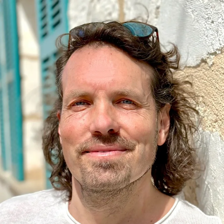 Timm Korth mit lockigen haaren und bart, nahaufnahme porträt vor heller wand