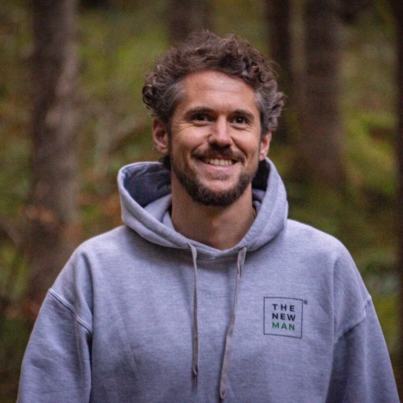 Moritz Ertinger Portrait, junger Mann lächelnd in grauem Hoodie mit 'THE NEW MAN' Schriftzug